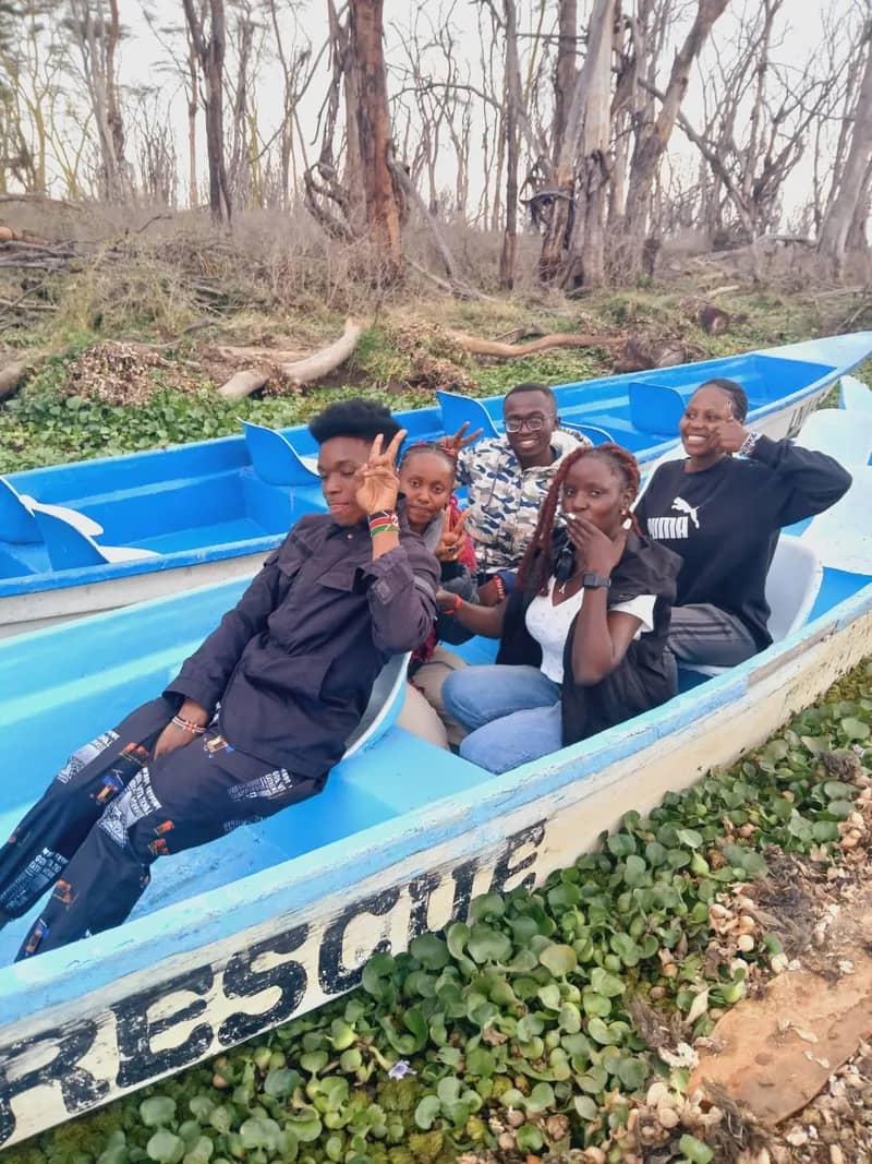 A HikeQuest group sitting in a blue boat at the lakeshore among water hyacinth