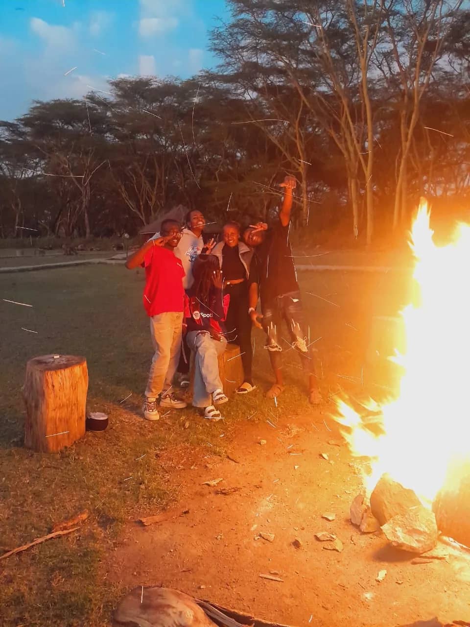 A HikeQuest group posing beside a bonfire at dusk with sparks flying