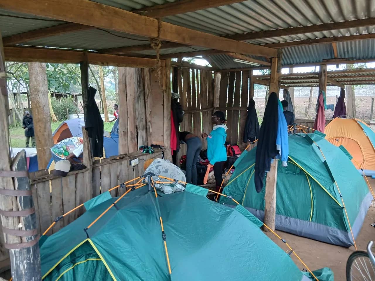 A HikeQuest camp with tents pitched under a timber shelter and the group among them