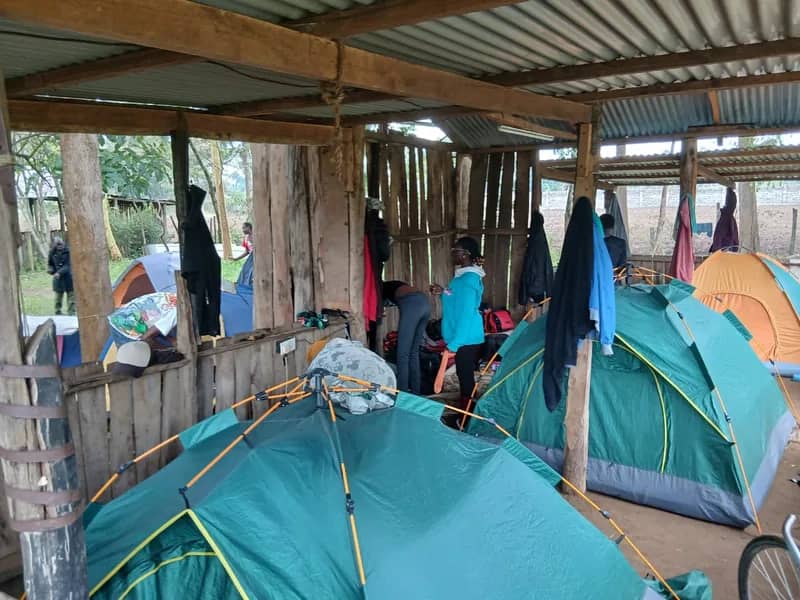 A HikeQuest camp with tents pitched under a timber shelter and the group among them