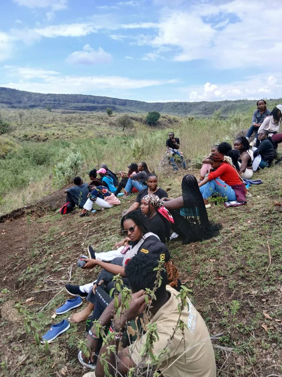 A HikeQuest group resting on a grassy crater slope, one of them in a branded shirt