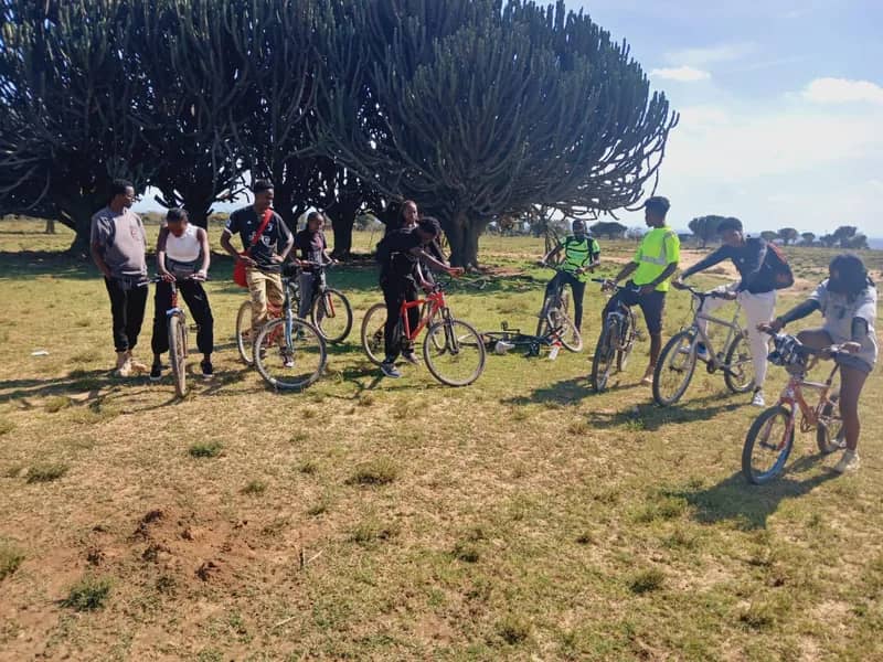 A HikeQuest cycling group with their bikes under candelabra euphorbia trees on the Narok plains