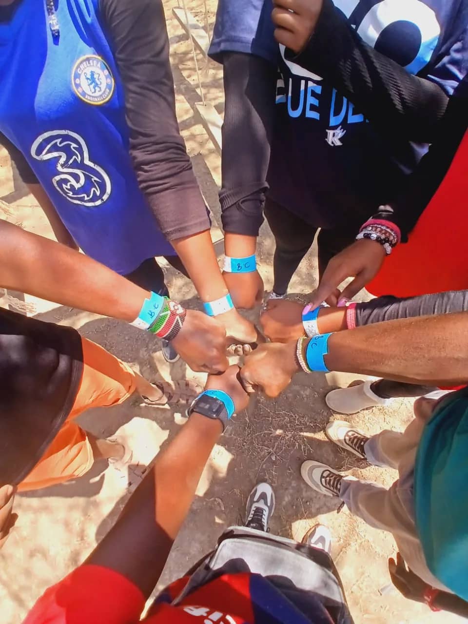 Looking down on a circle of HikeQuest adventurers touching fists, wristbands on