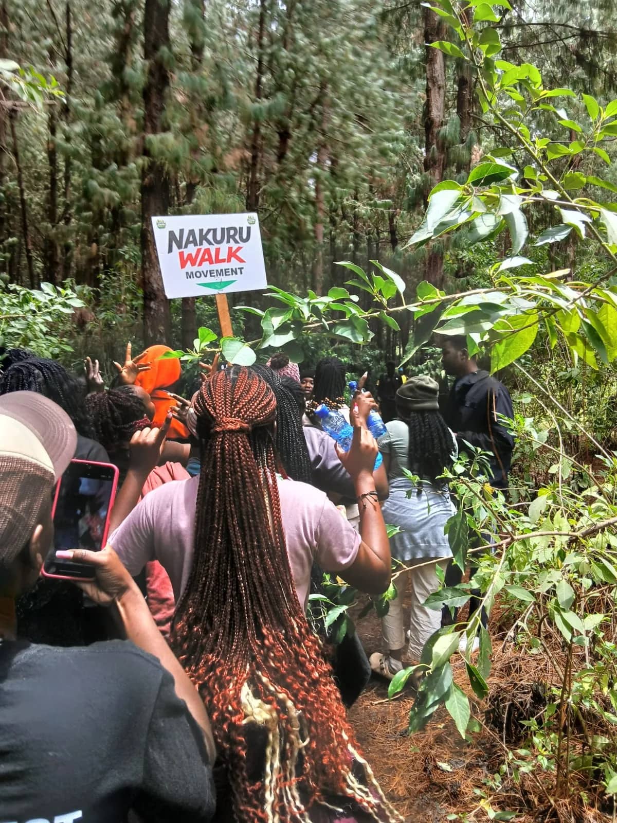 A HikeQuest group walking a forest trail behind a Nakuru Walk Movement placard