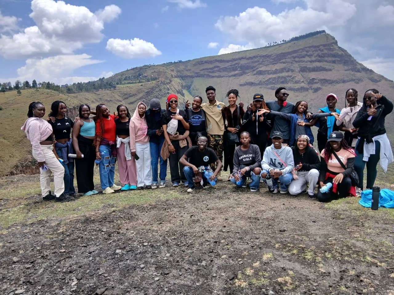 A large HikeQuest group of about twenty gathered on a hilltop with the escarpment behind them