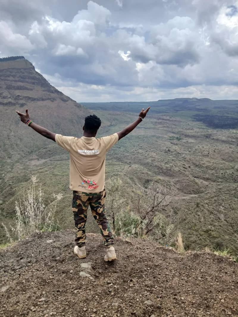 A HikeQuest guide in the khaki branded shirt standing arms wide on a crater rim