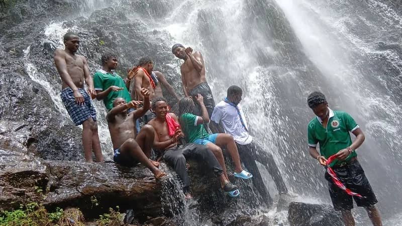 HikeQuest adventurers sitting and standing on wet rocks beneath a waterfall