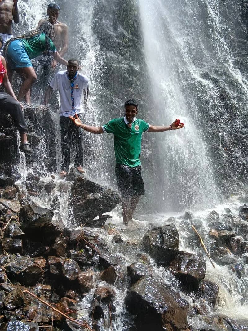A HikeQuest adventurer standing arms wide in the spray at the foot of a waterfall