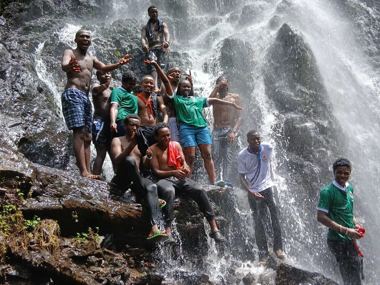 A HikeQuest group standing on the rocks under a waterfall with their arms raised